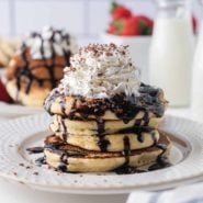 Short stack of chocolate chip pancakes with chocolate syrup and whipped cream.