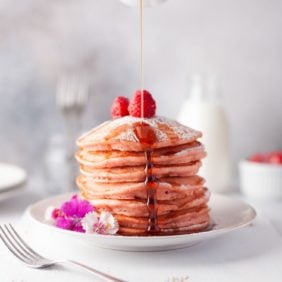 Beet pancakes with syrup being poured on them.