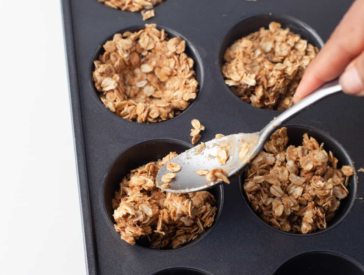 Spoon pressing oat mixture into muffin tin.