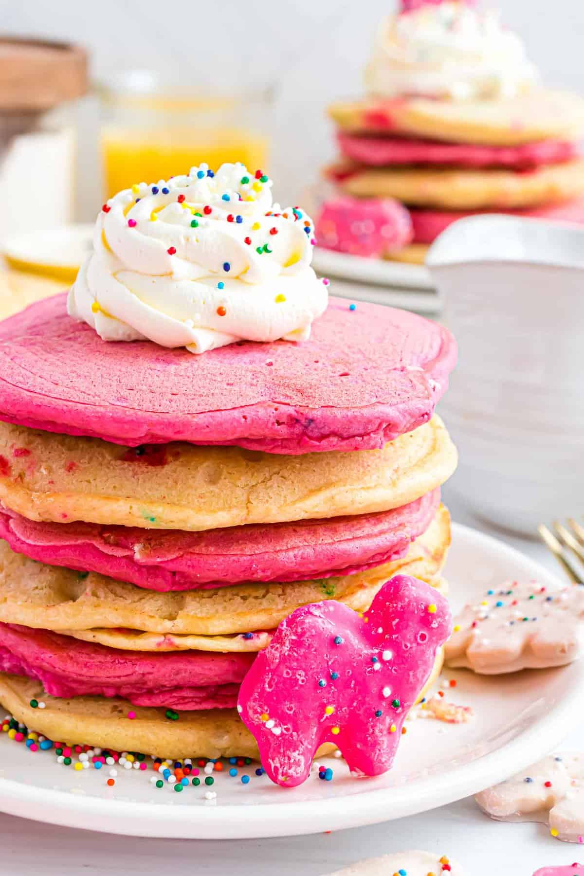 White and pink frosted animal cracker pancakes topped with whipped cream.