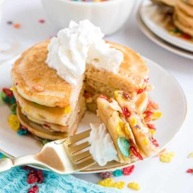 Stack of fruity pebbles pancakes with whipped cream.