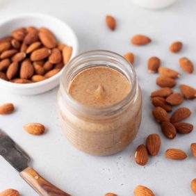 Homemade almond butter in a small jar, surrounded by almonds.
