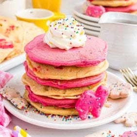 Frosted animal cracker pancakes stacked high with whipped cream.