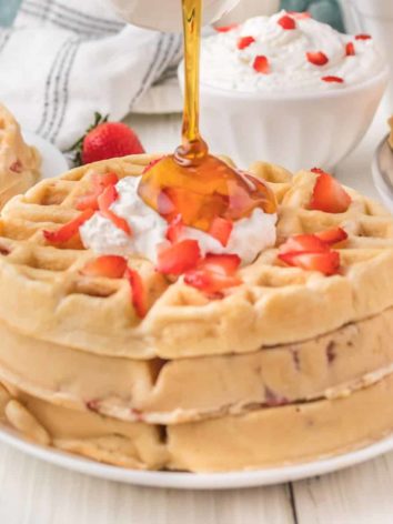 Syrup being poured on strawberry waffles.