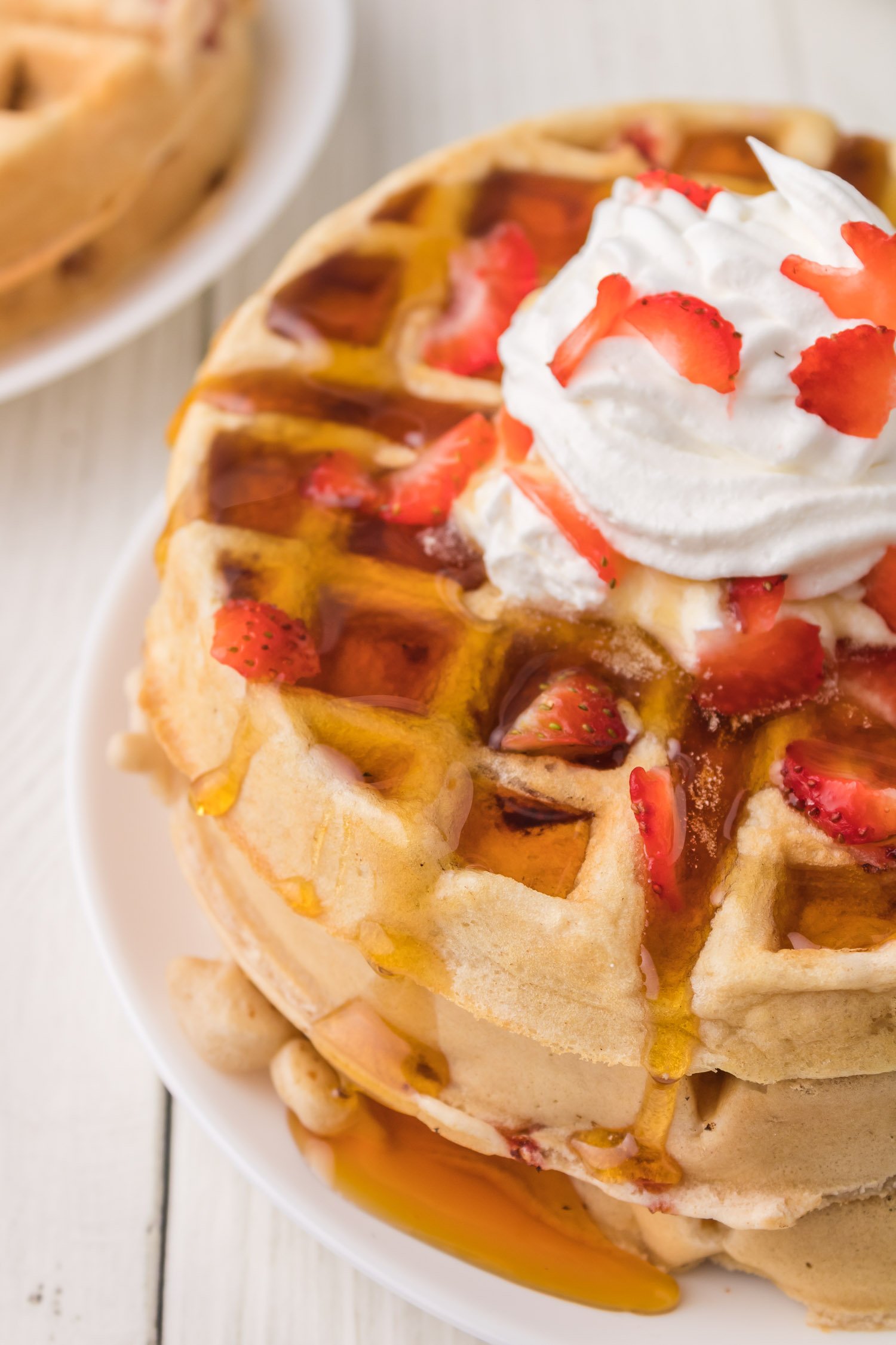 Large strawberry waffles, stacked with syrup, whipped cream, strawberries.